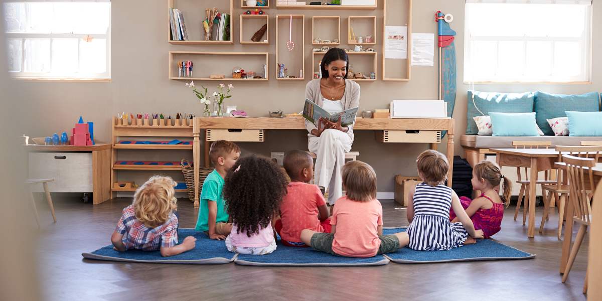 Teacher At Montessori School Reading To Children At Story Time